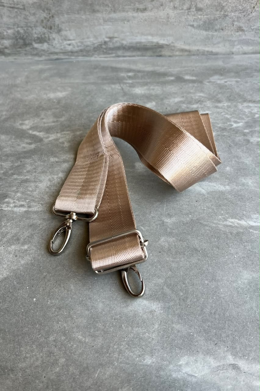 A champagne gold nylon shoulder strap with silver metal swivel clips and a slider buckle, laid out on a gray textured surface.