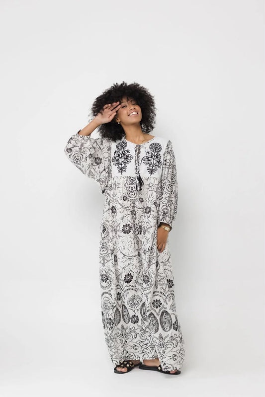A woman modeling a long-sleeved maxi dress with a black and white paisley pattern, standing against a solid light gray background.
