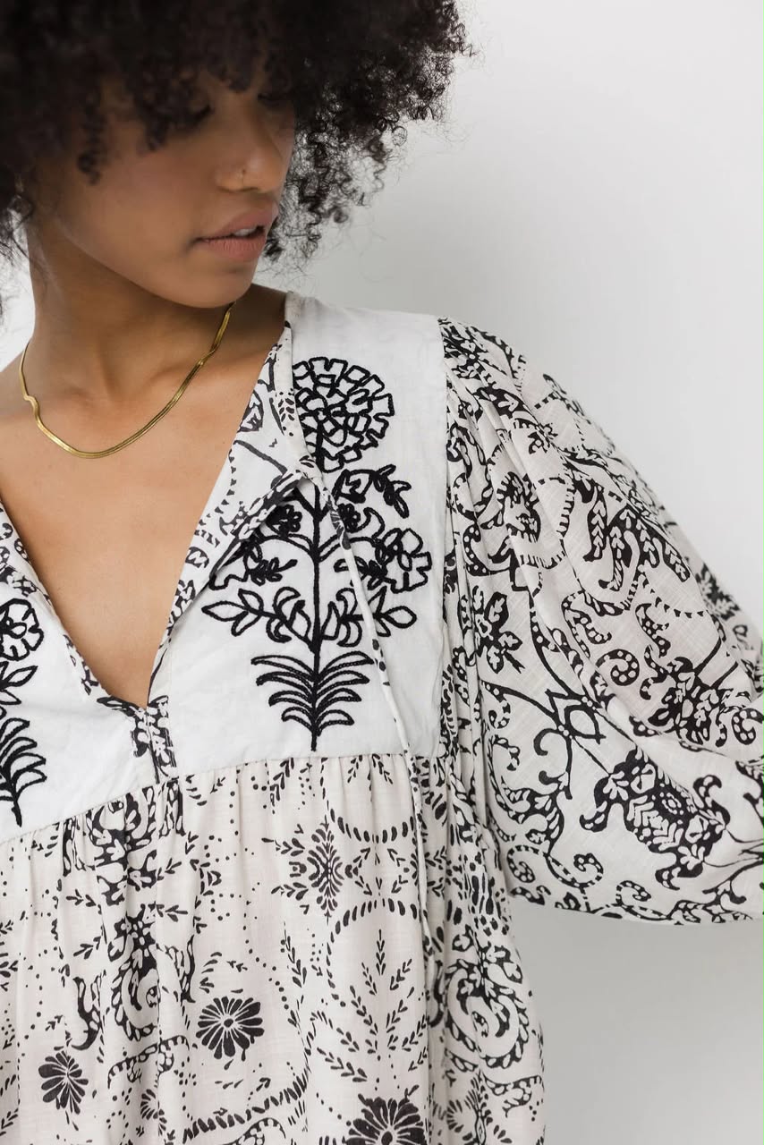 A close-up of a woman wearing a white blouse with black floral and animal prints, featuring a V-neckline and long sleeves.