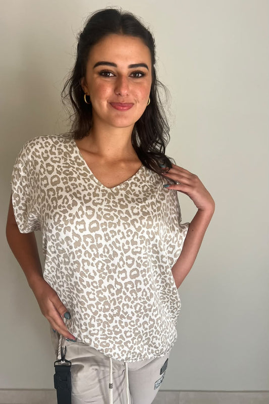Woman wearing a relaxed-fit white short-sleeve top with a V-neckline and an all-over beige leopard print, paired with light-coloured bottoms for a stylish, casual everyday look.
