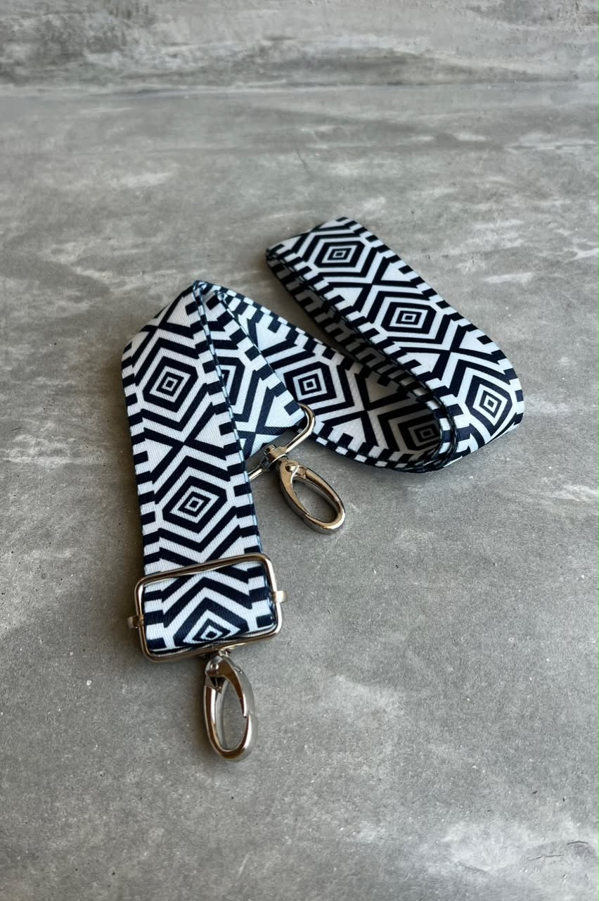 A blue and white geometric patterned fabric strap with silver-tone metal hardware, including a buckle, clips, and a swivel ring, displayed on a gray textured surface.