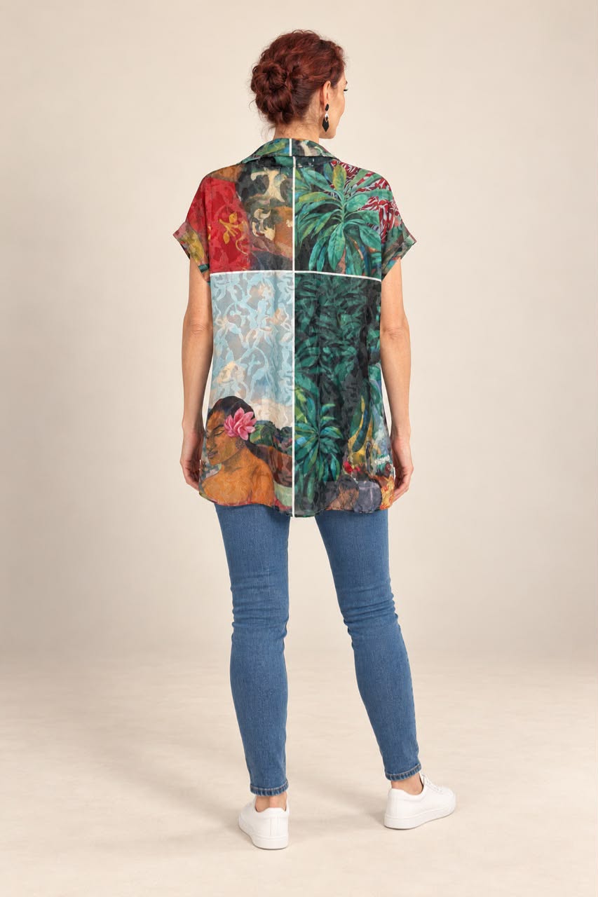 A woman viewed from the back wearing a short-sleeve button-up shirt with a colorful patchwork print featuring tropical foliage and portraits, paired with blue skinny jeans and white sneakers, against a plain beige studio background.