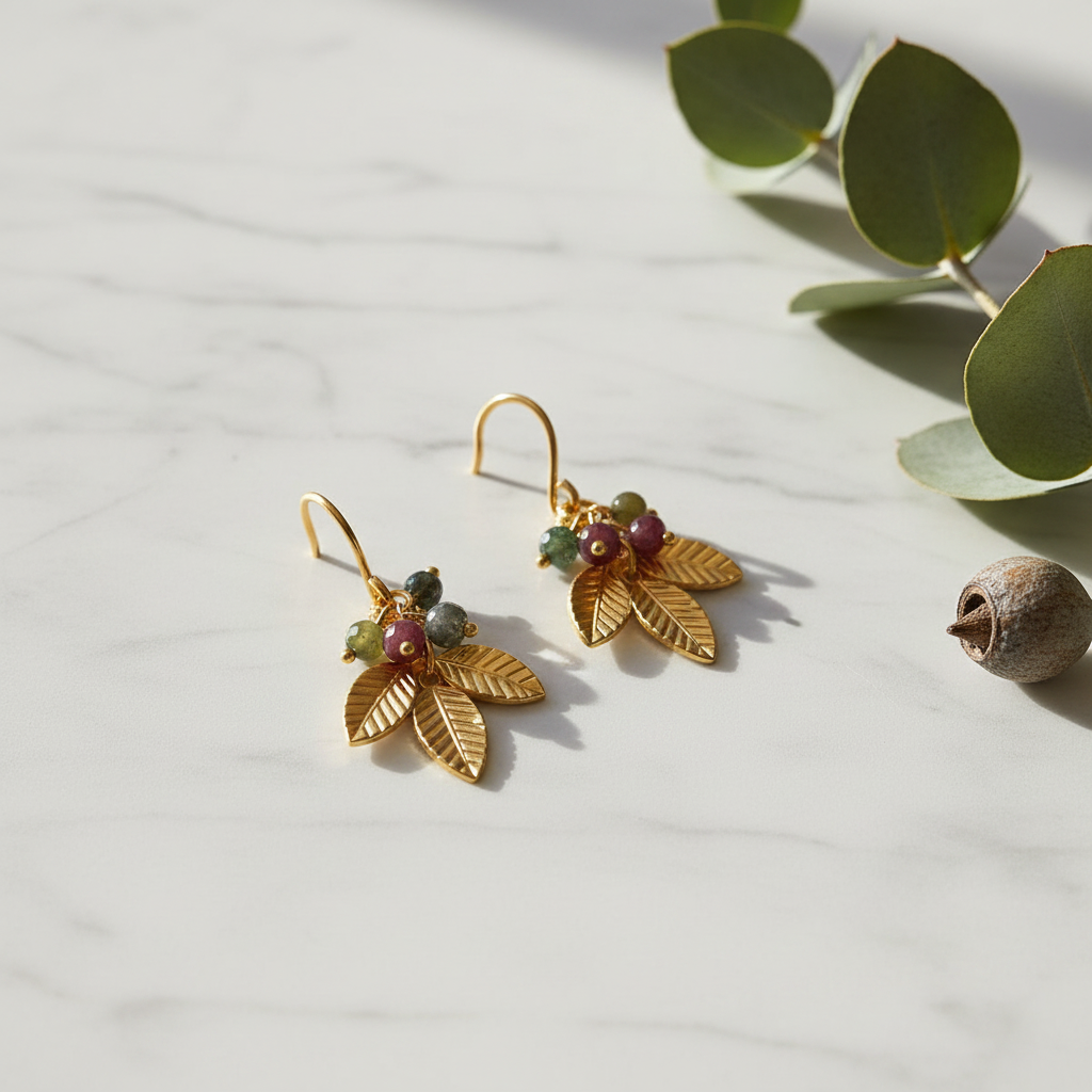 Gold leaf and tourmaline bead cluster earrings on marble surface with eucalyptus sprig