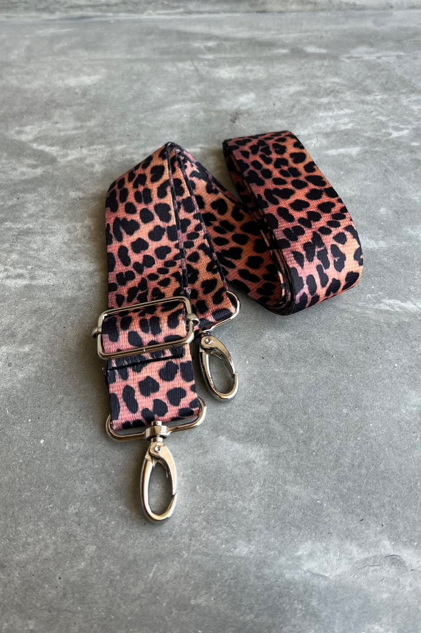 A leopard print shoulder strap featuring silver metal hardware, displayed on a gray textured surface.