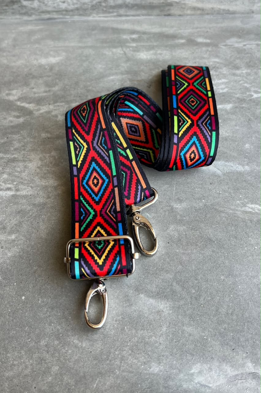 A multicolor geometric patterned fabric strap with silver-tone metal hardware, displayed on a gray textured surface.