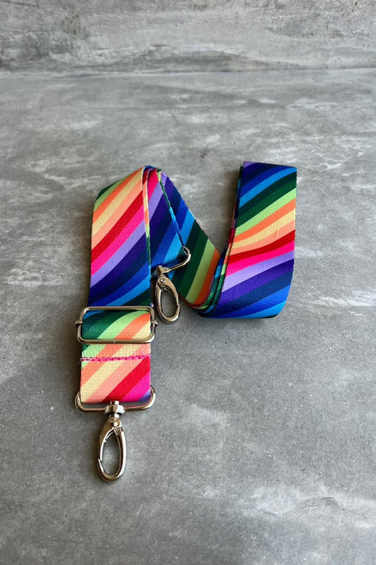 A vibrant rainbow-striped fabric strap with silver metal hardware, laid flat on a gray textured surface.