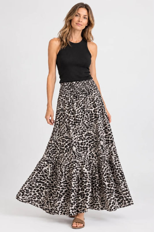 A woman modeling a sleeveless black top and a high-waisted, tiered black and beige leopard-print maxi skirt against a light gray studio background.